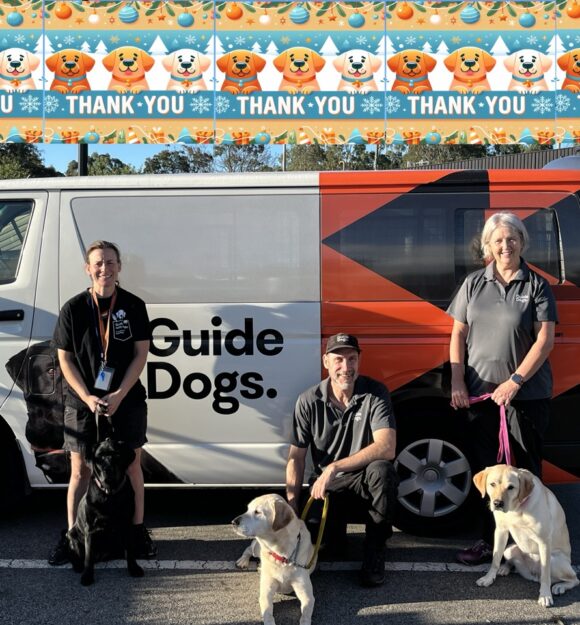 Three Guide Dogs Victoria staff members accompanied by three Labrador dogs standing in front of the Guide Dogs Van.