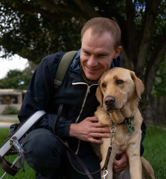 Brendan a GDV ambassador is hugging his Guide Dog Gunner outside in the park.