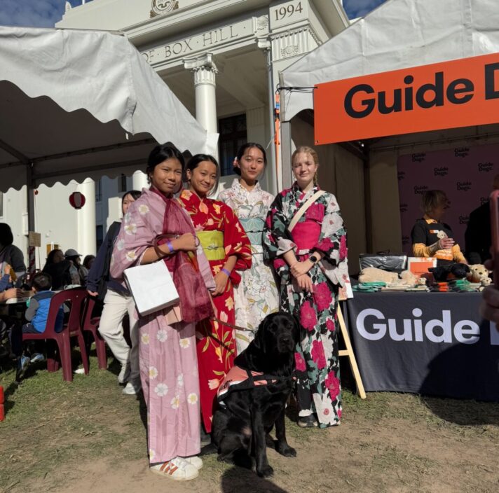 Four attendees wearing colourful kimonos at the Japan Festival 2025, with a black guide dogs wearing a harness.