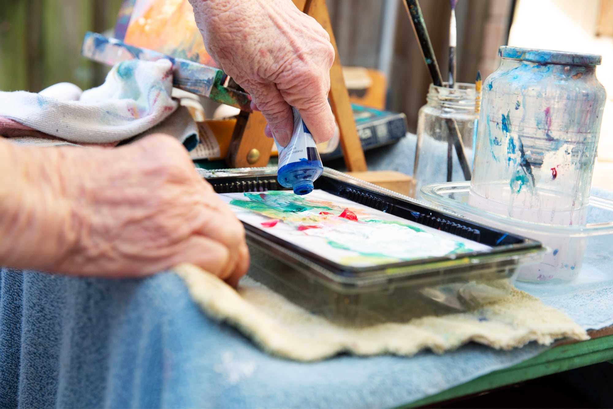 An older adult squeezing paints out of a tube into a paint tray.