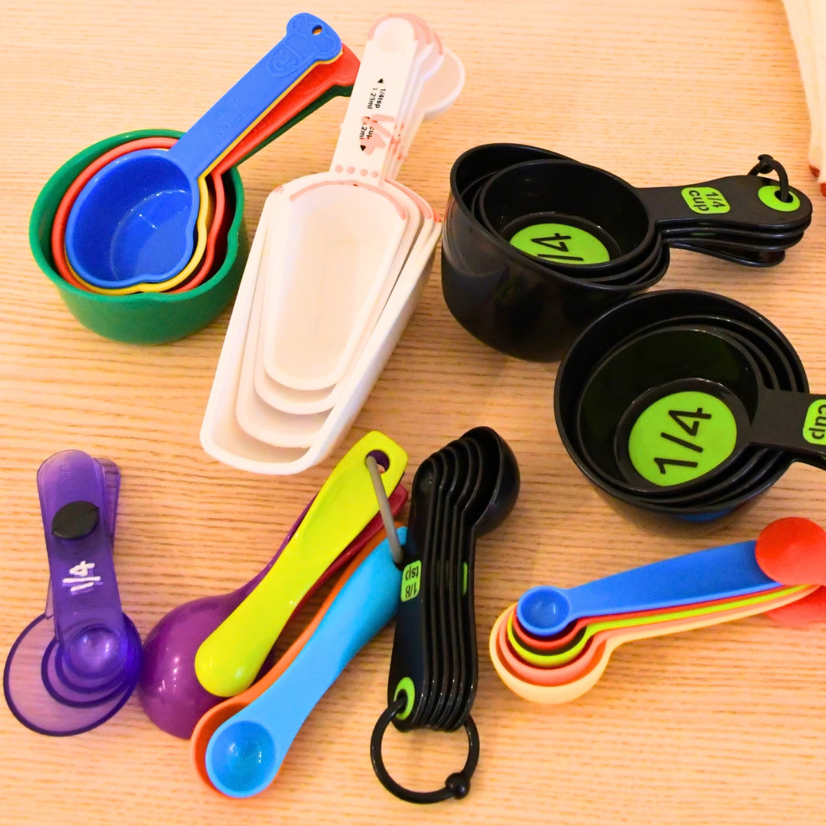 A variety of colourful measuring cups and measuring spoons arranged on a wooden table.