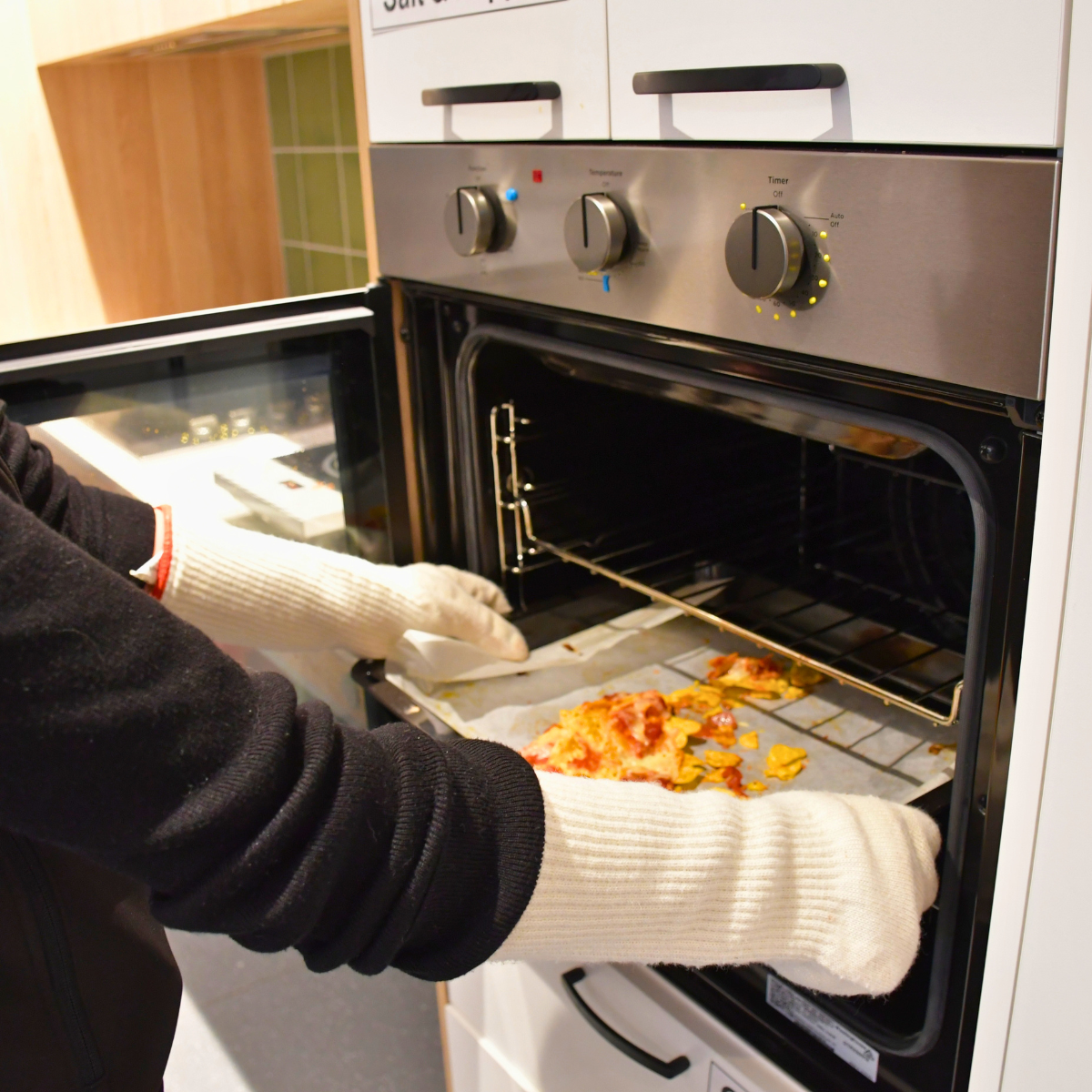A person wearing oven gloves placing a tray of cooked food into an open oven.