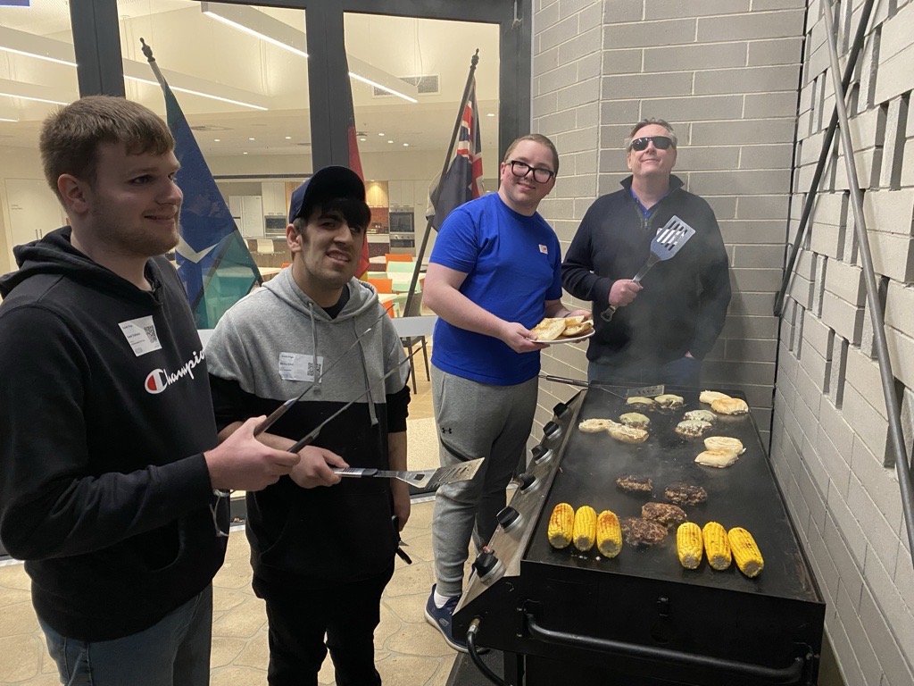 From the left – Sam, Ricky, Sebastian and Rory around the BBQ, engaging in a BBQ skills lesson – cooking burgers together