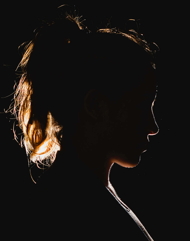 A woman's profile is backlit by light, her face is cast in shadow