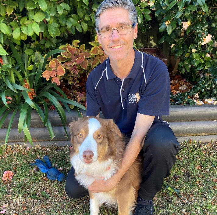 A man crouching next to a dog, smiling at the camera.