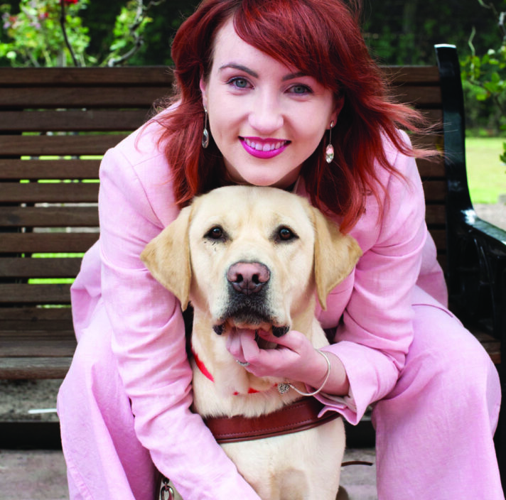 Client Ingrid sitting with her arms around yellow labrador Guide Dog Banner