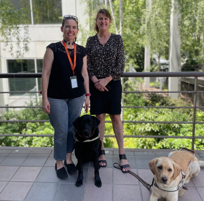Erin and Melaine standing on a balcony with their Guide Dogs in front of them