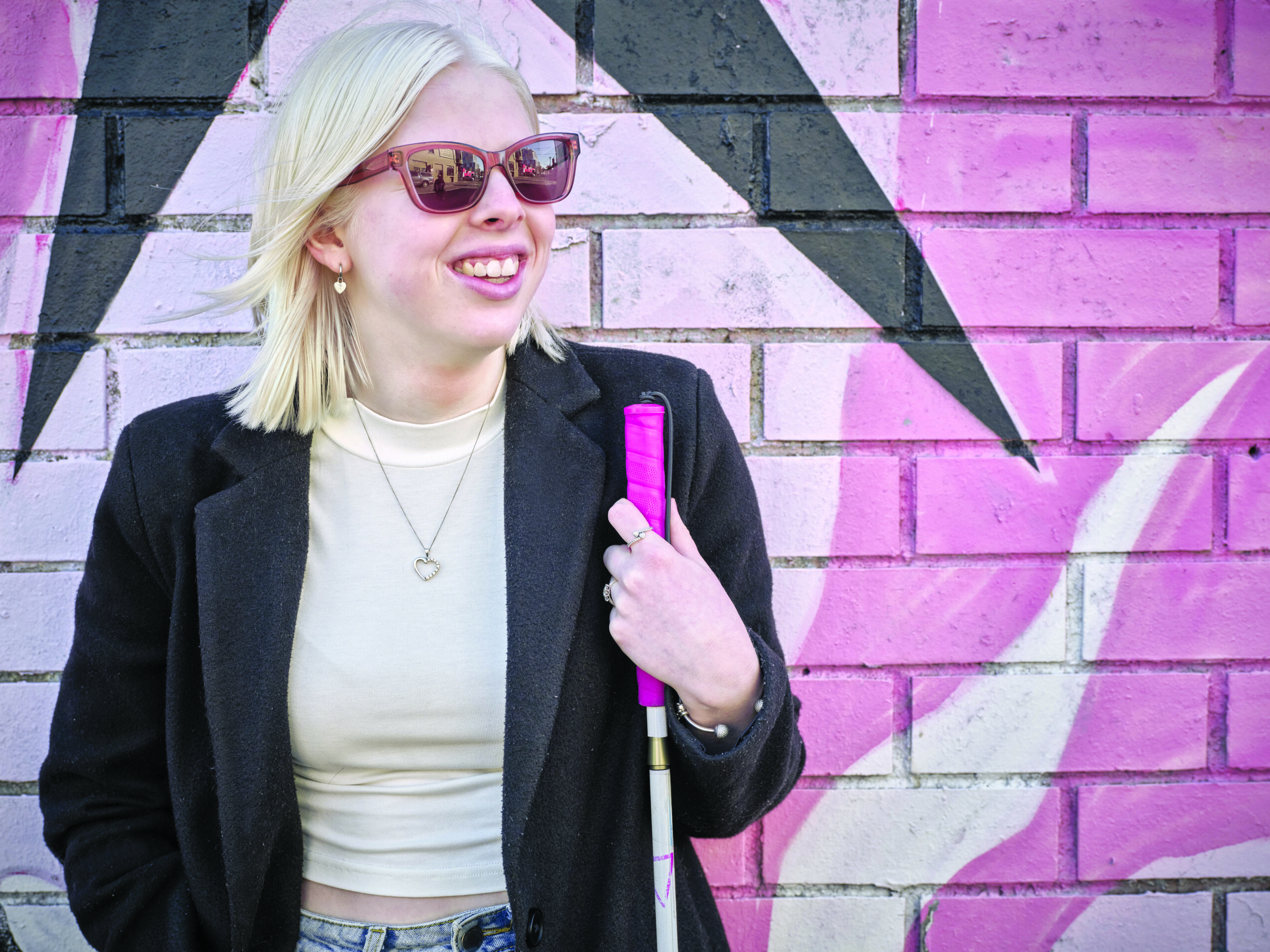 A young person with a pink cane standing in front of a pink wall.