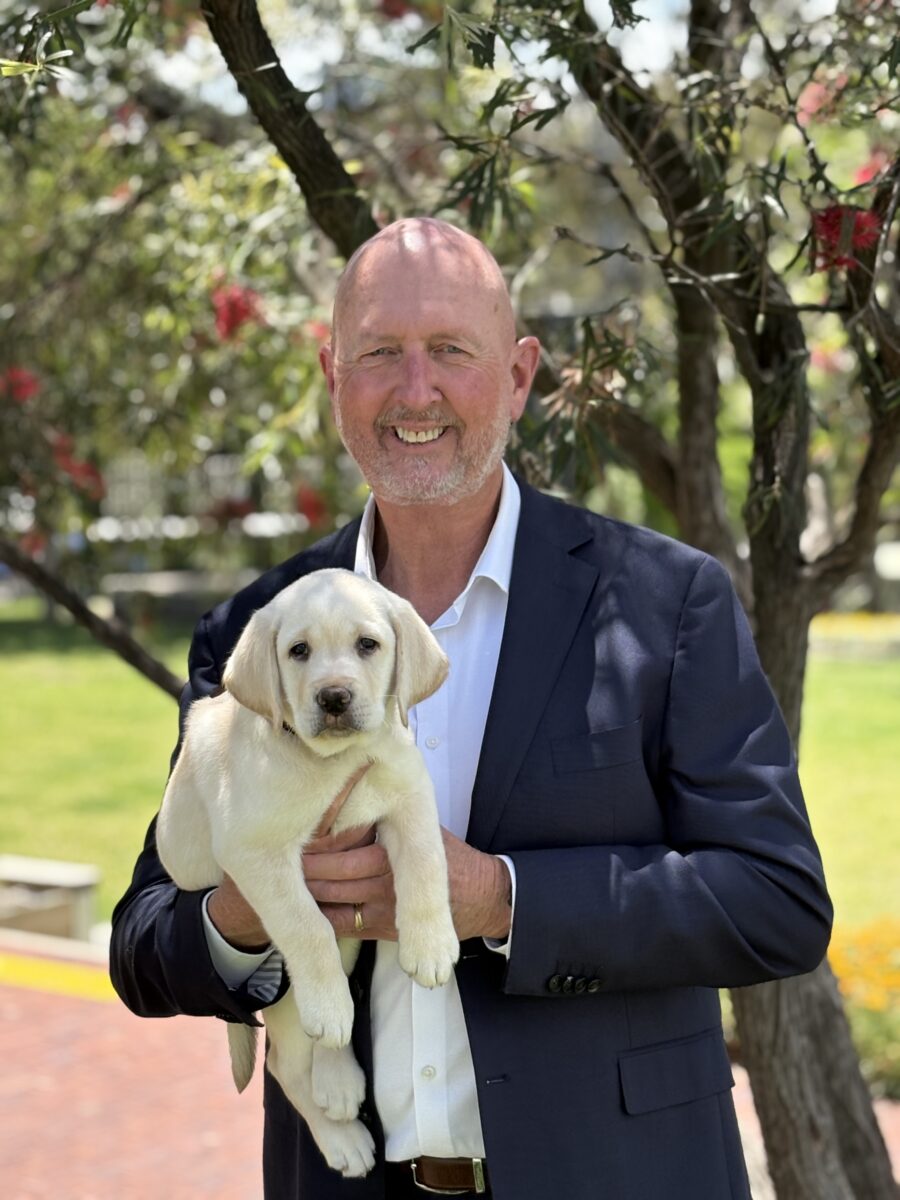 Michael Boyce holds a yellow lab puppy smiling at the camera.