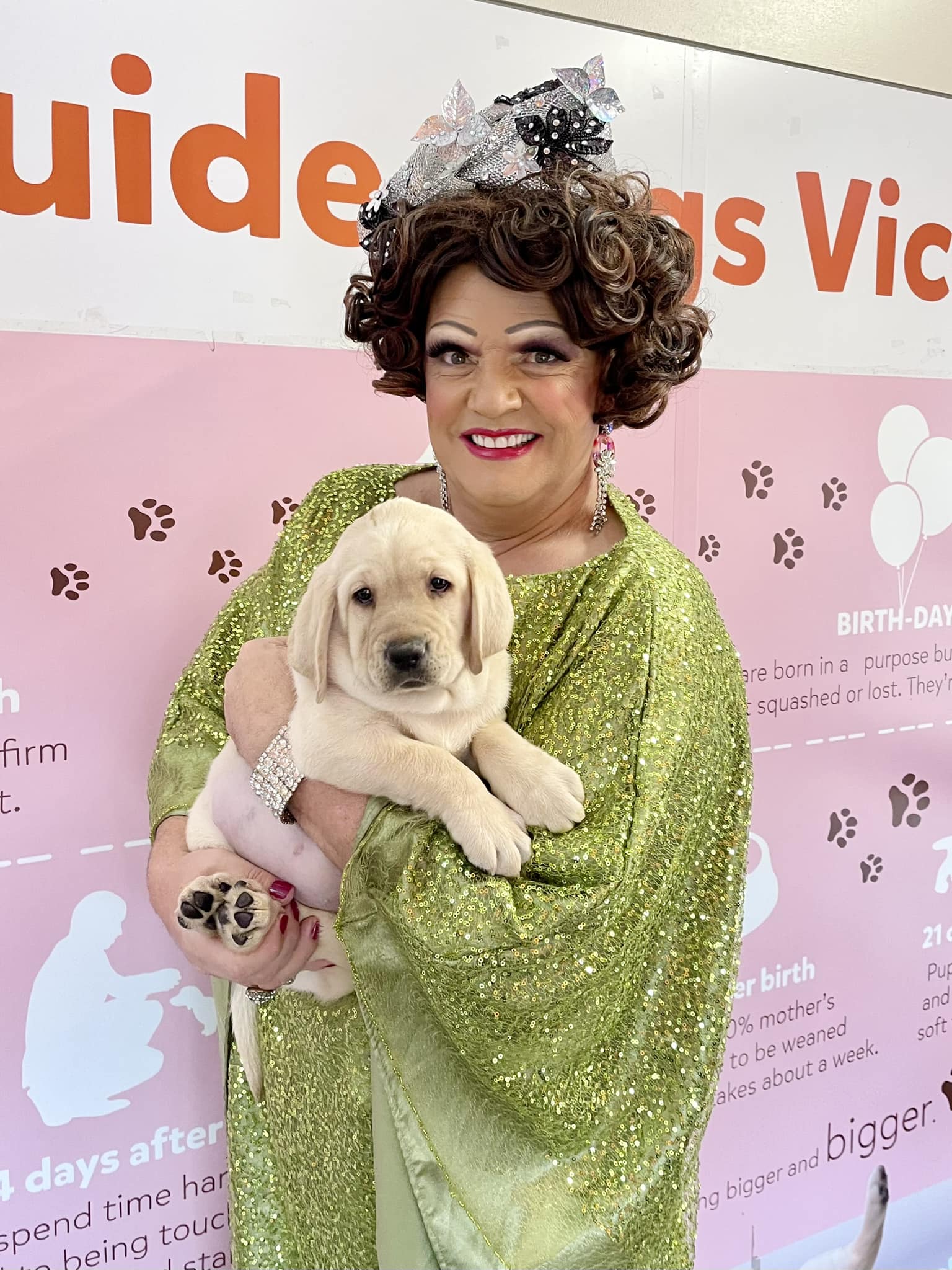 Dolly in a bright green dress and silver headpiece, holding a yellow Labrador puppy with a big smile on her face.