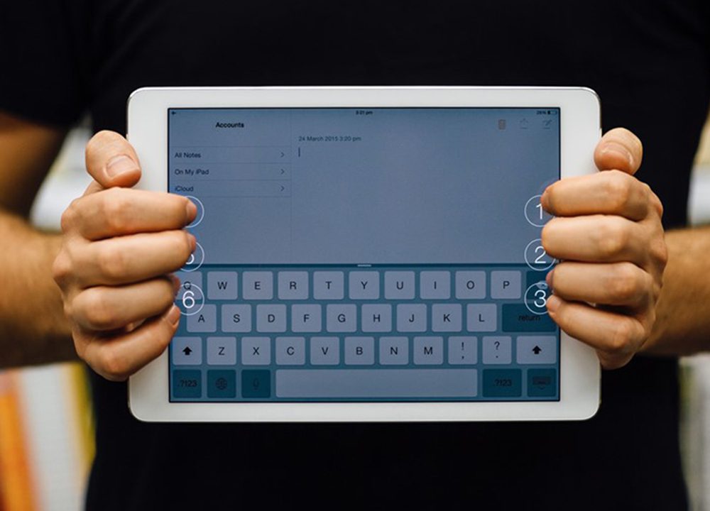 A person is holding an ipad. They are standing behind it, holding the device landscape with the screen to the camera