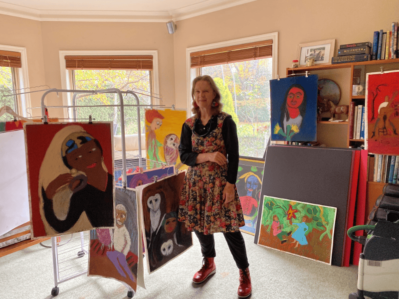 Artist Claire Hogan standing in her art studio, surrounded by pieces of her work.