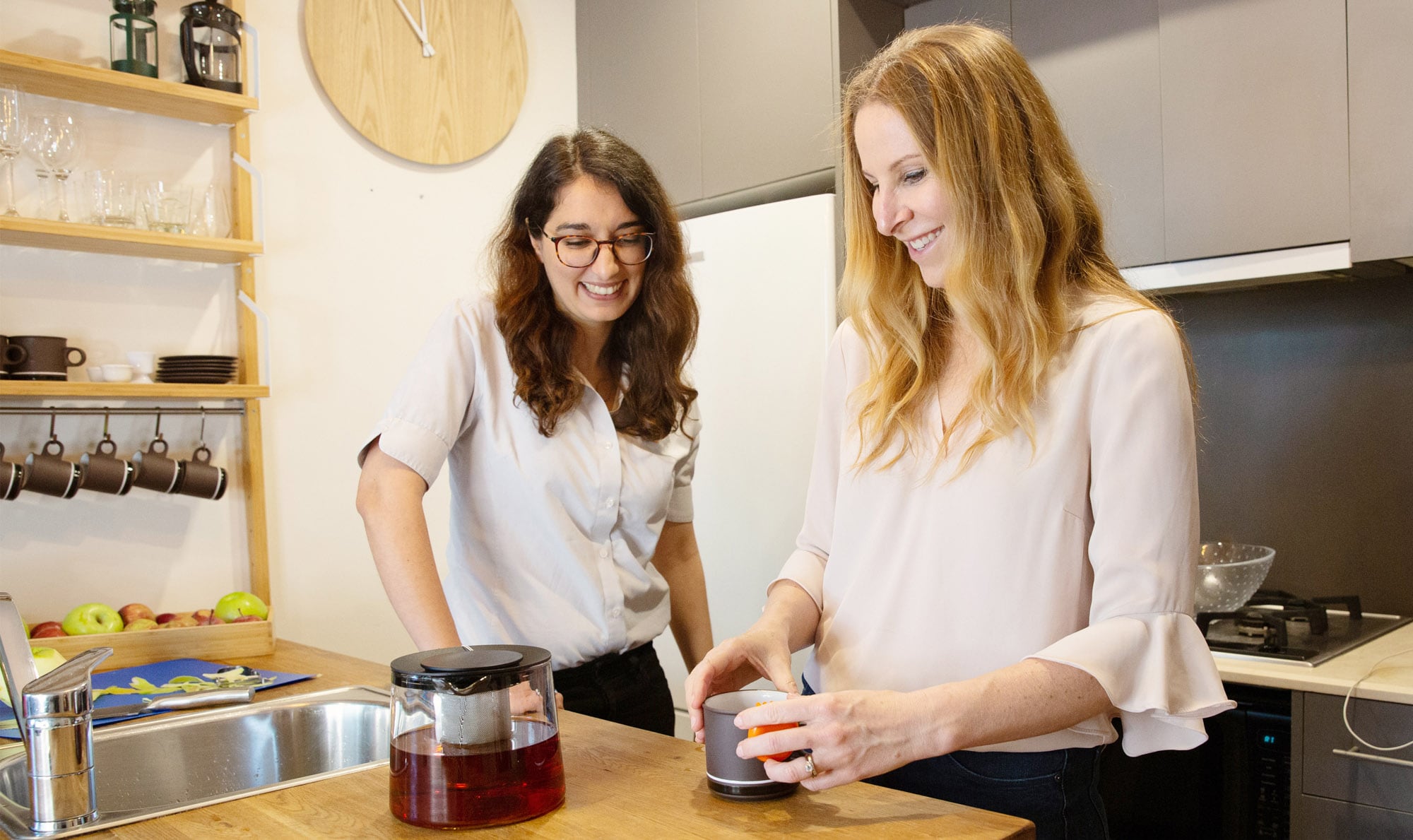 Two people inside in the kitchen. One is making tea while the other is watching on.