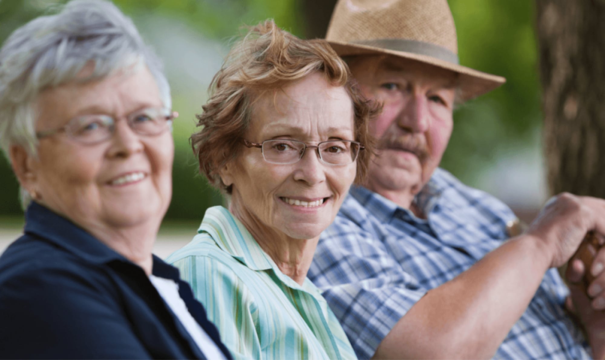 Three older adults seated in a row all looking at the camera smiling.