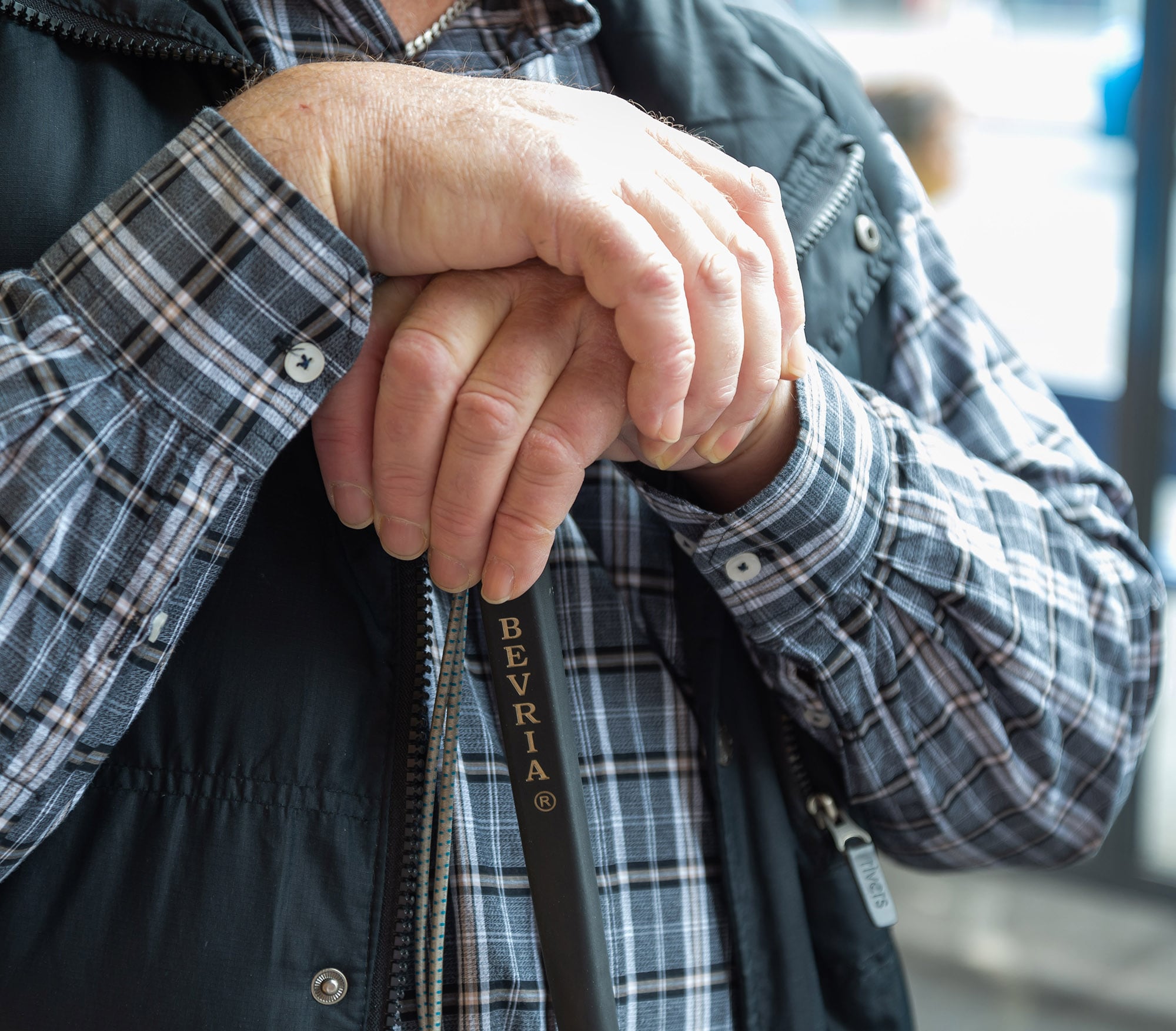 Close up of two hands resting on the top of a white cane.