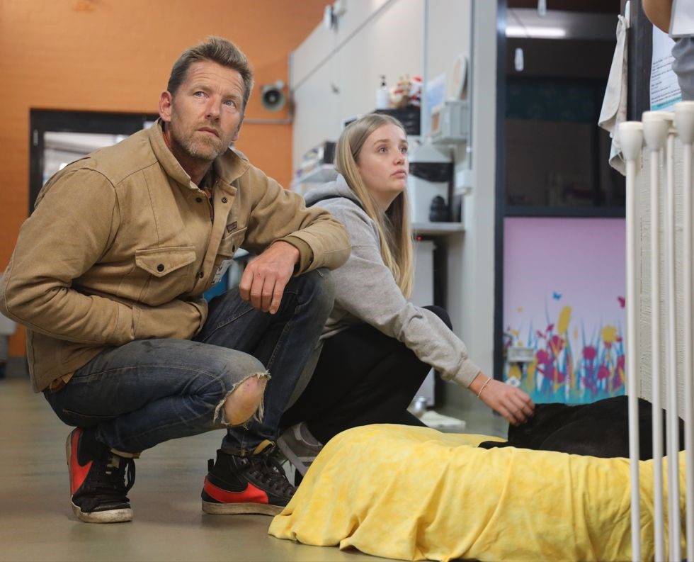 Joost and his daughter kneeling next to a bed where a black Labrador puppy is sleeping.