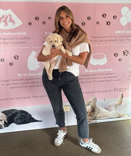 Lauren Phillips standing in the Guide Dogs nursery, holding a yellow Labrador puppy.