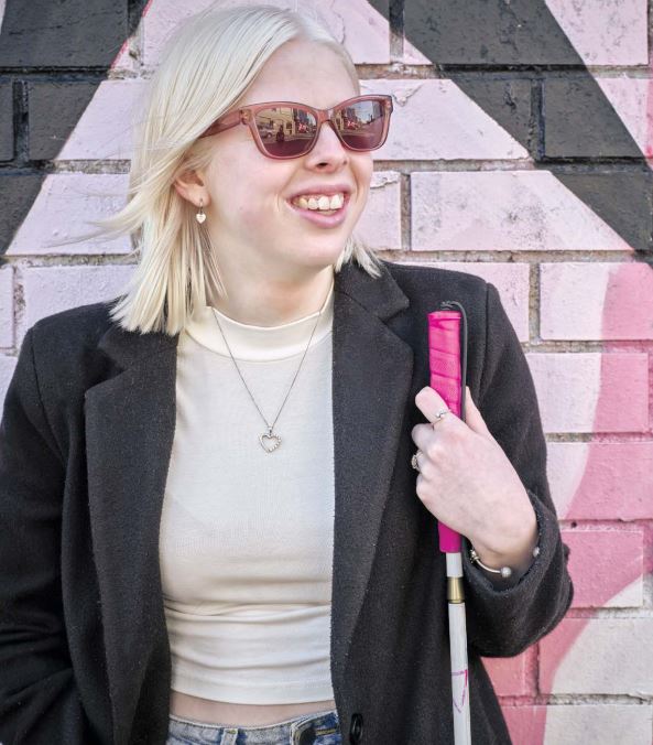 Client Lucy holding her cane standing in front of a painted wall