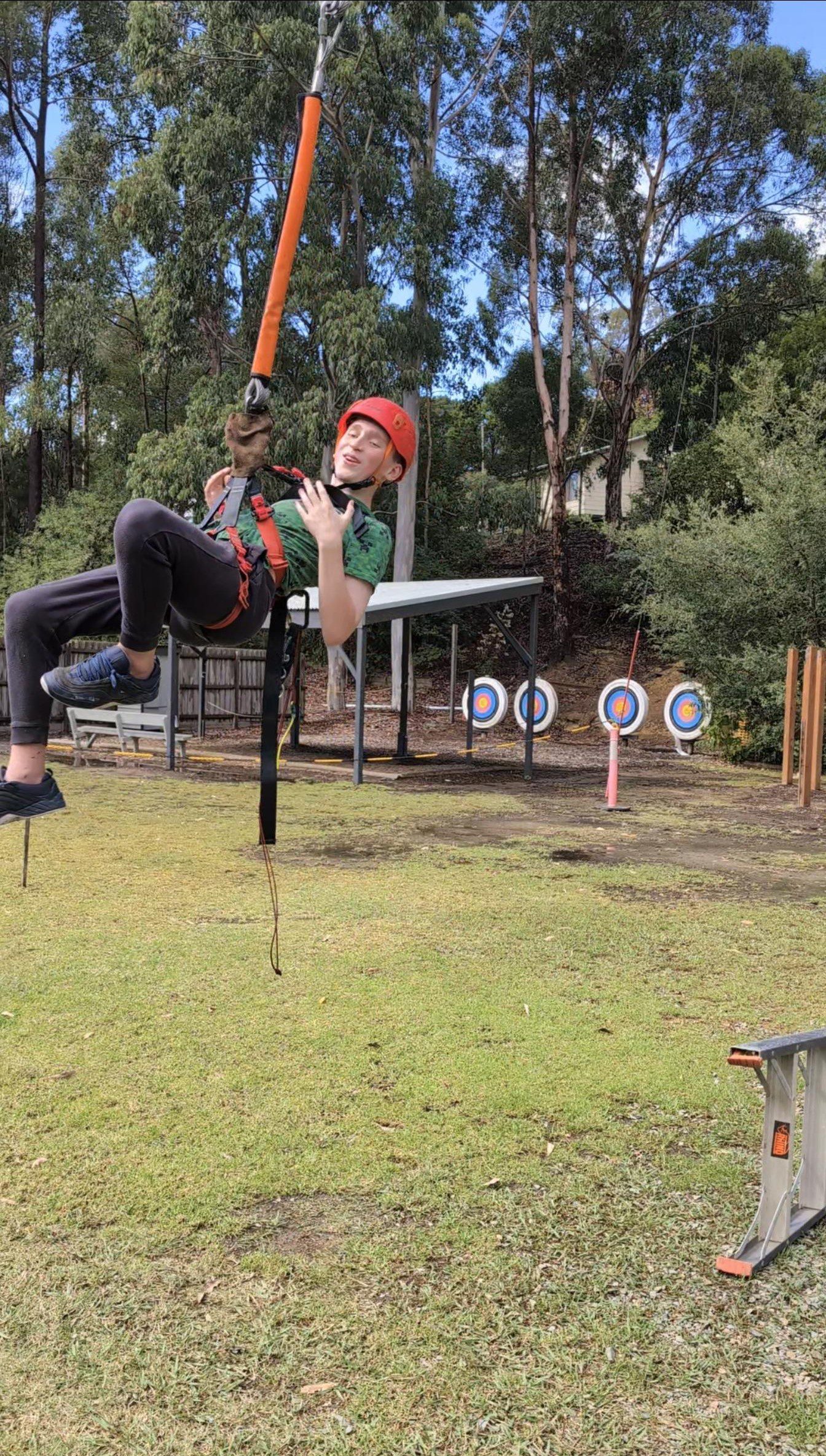 A participant wearing a red helmet, dangling from the flying fox with a smile on his face.