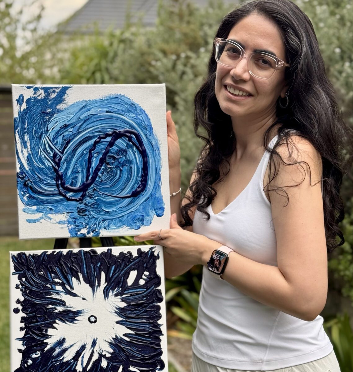 Noora Remi smiling holding up two pieces of her artwork.
