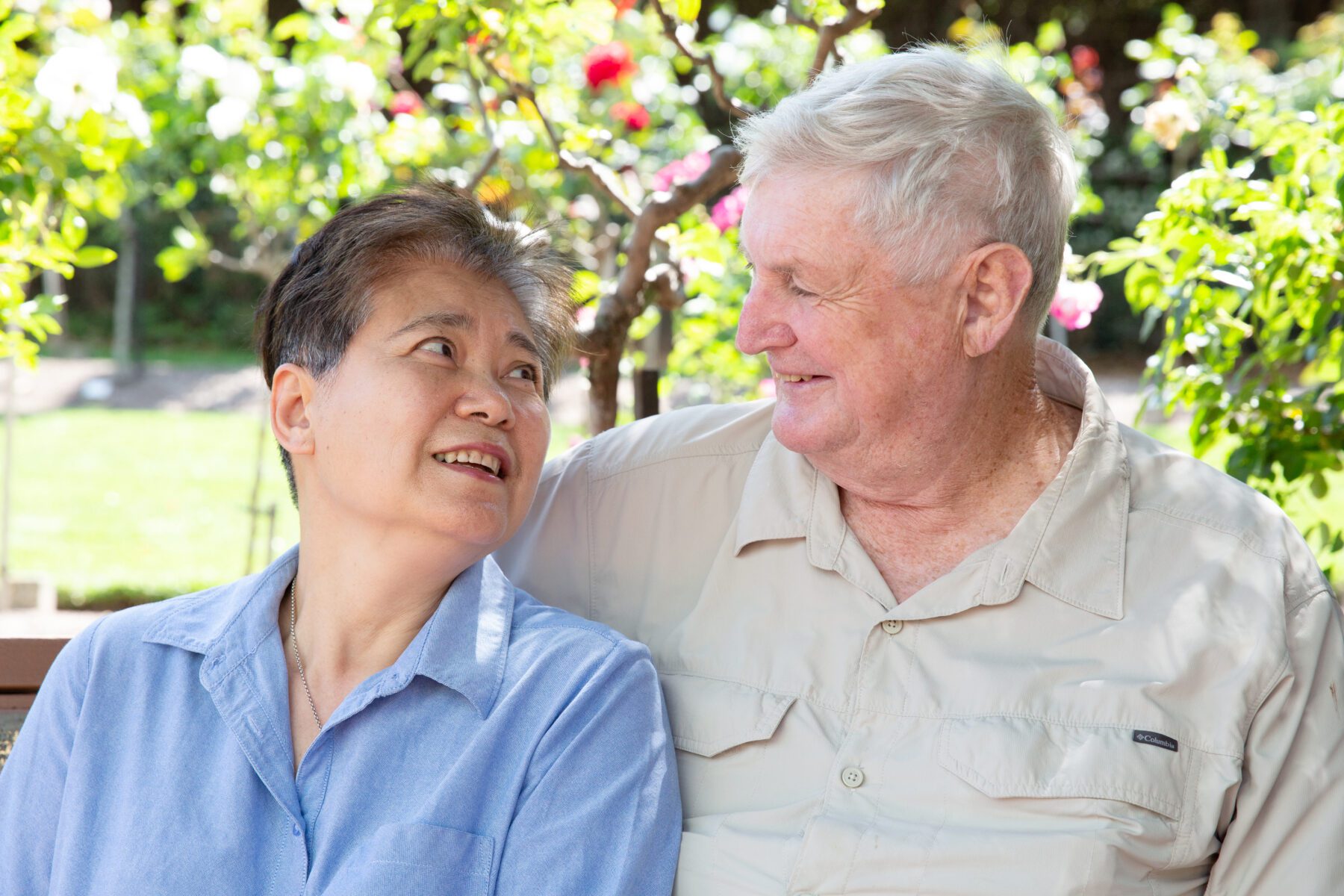 An older couple in a garden setting look into each others eyes.
