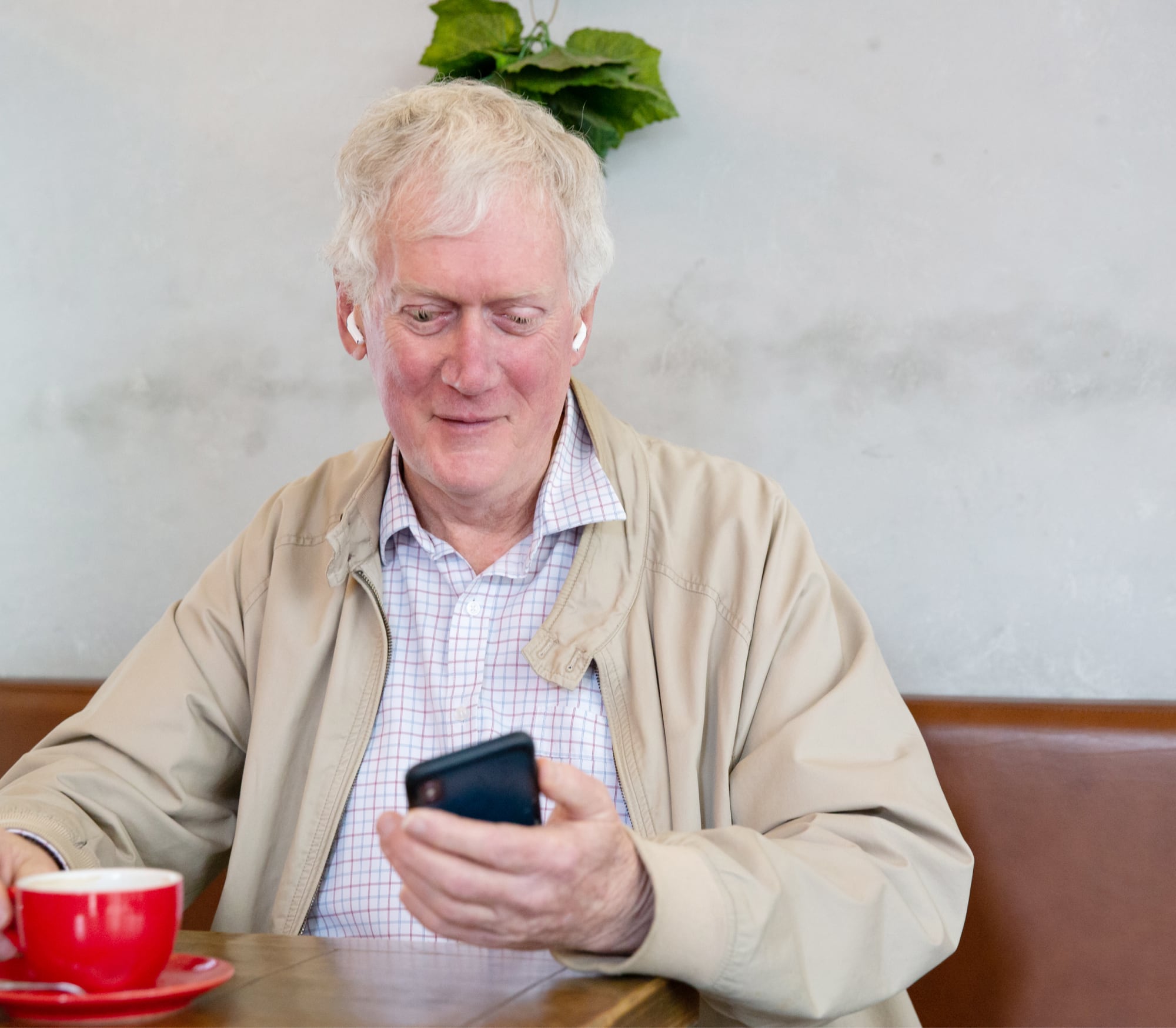 An older adult man sitting at a cafe looking at their phone.
