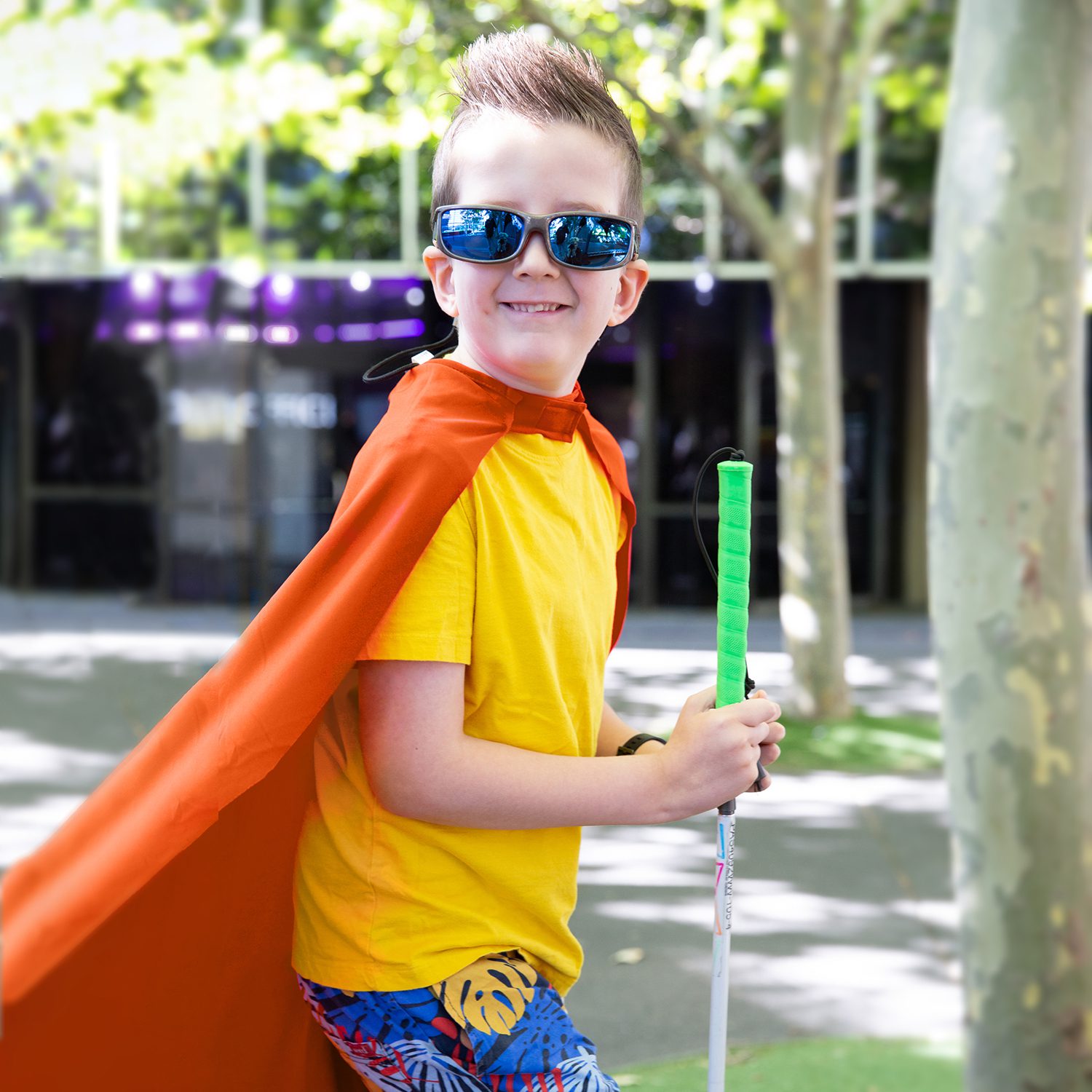 A child wearing a red superhero cape, proudly holding a cane