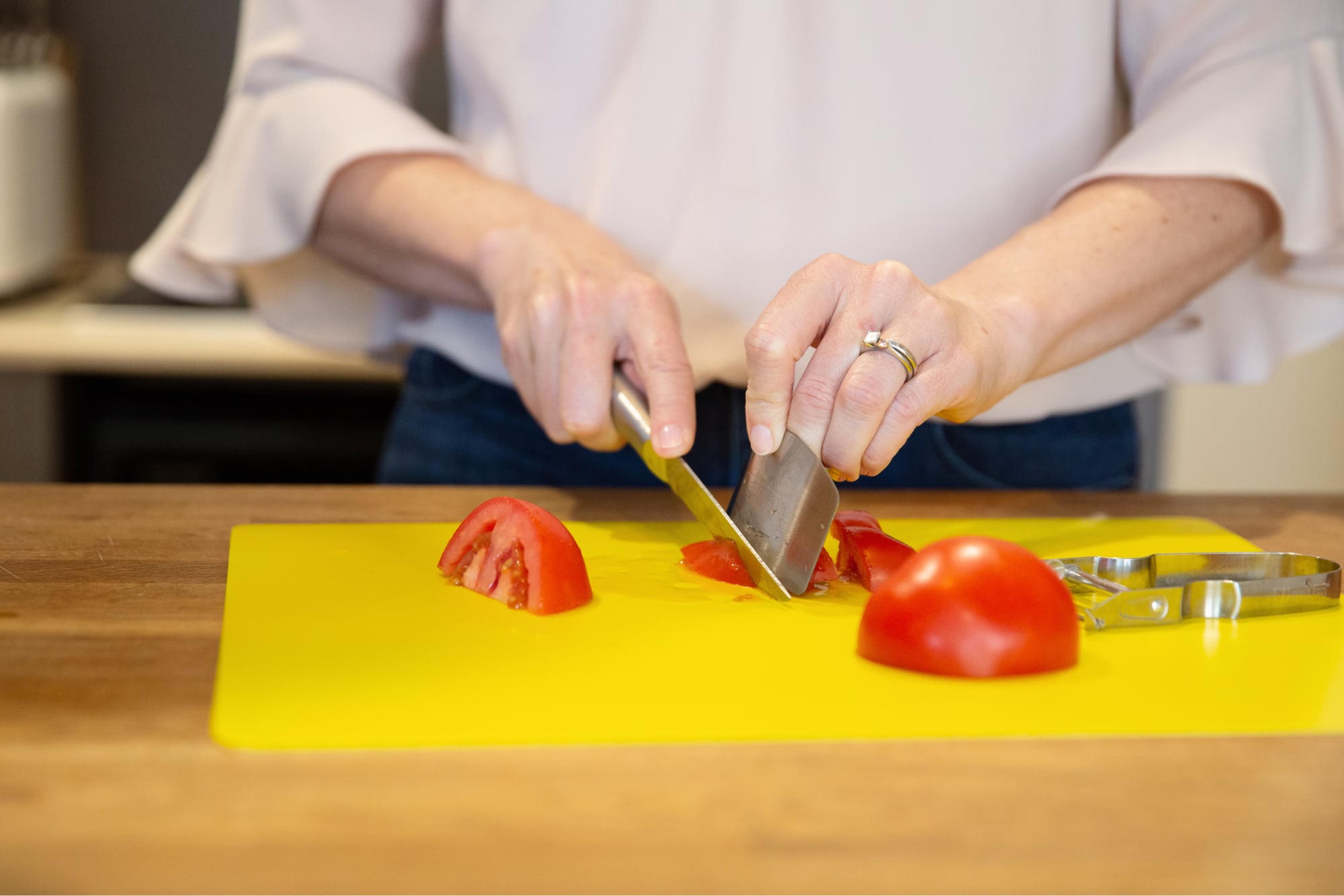 Person's hands chopping some tomatoes on a yellow chopping board.