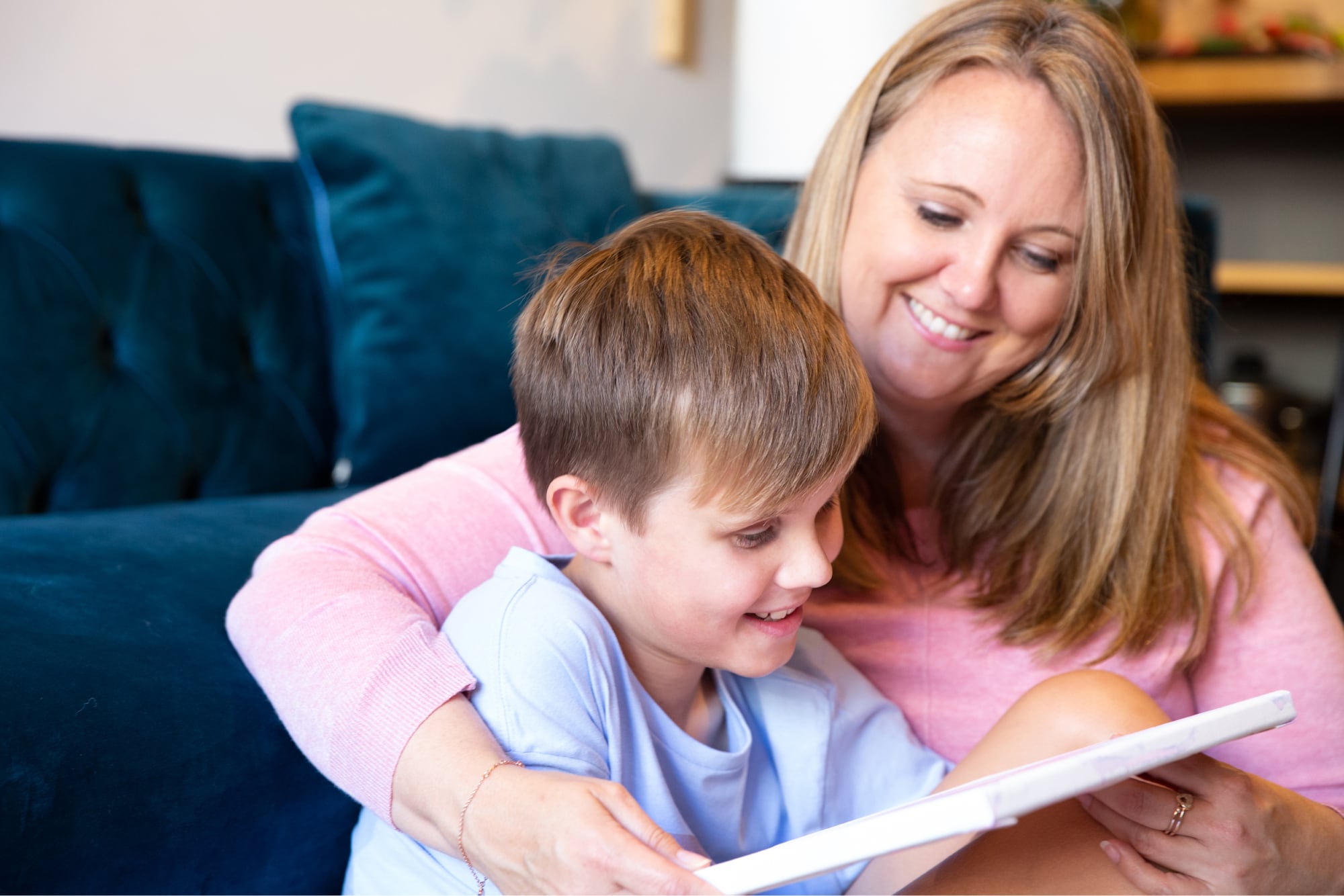 A woman wraps her arms around a young boy as they read a book together