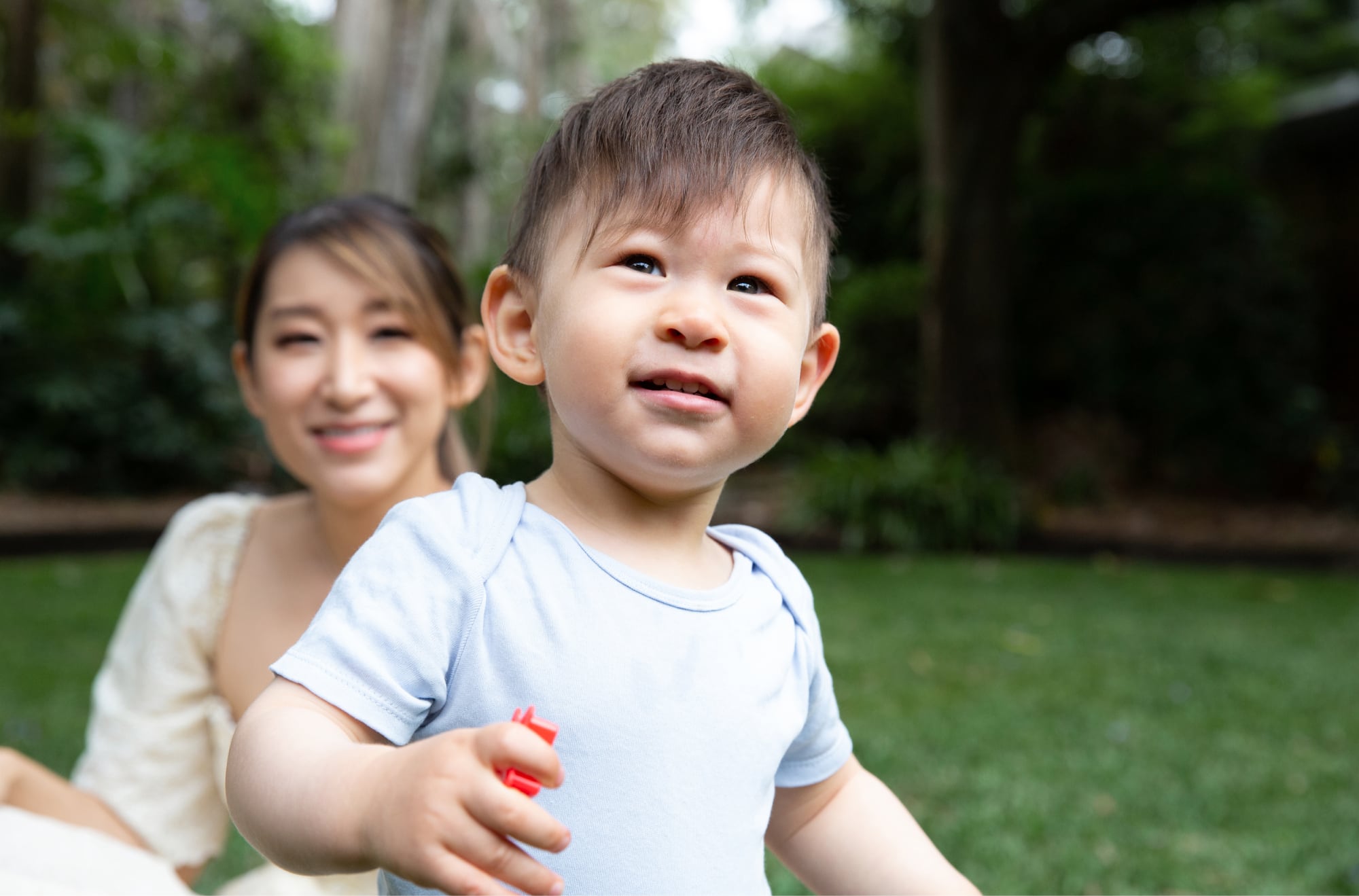 A young child playing outside with the mother watching in the background.