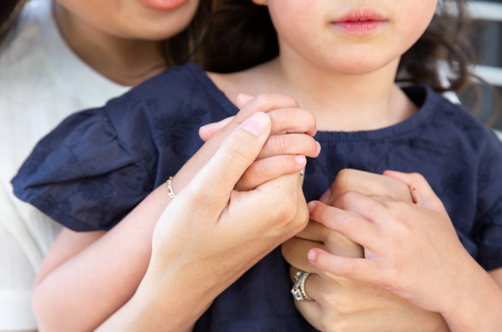 A close up of a mother cuddling a young child from behind, their hands are embraced.