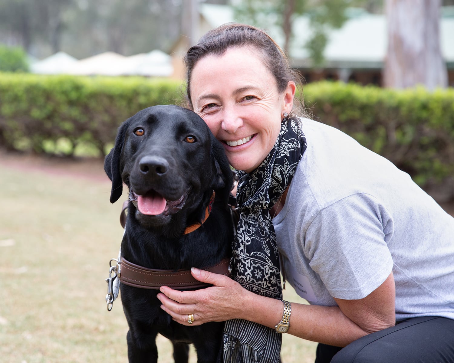 A woman crouches next to a black Labrador.
