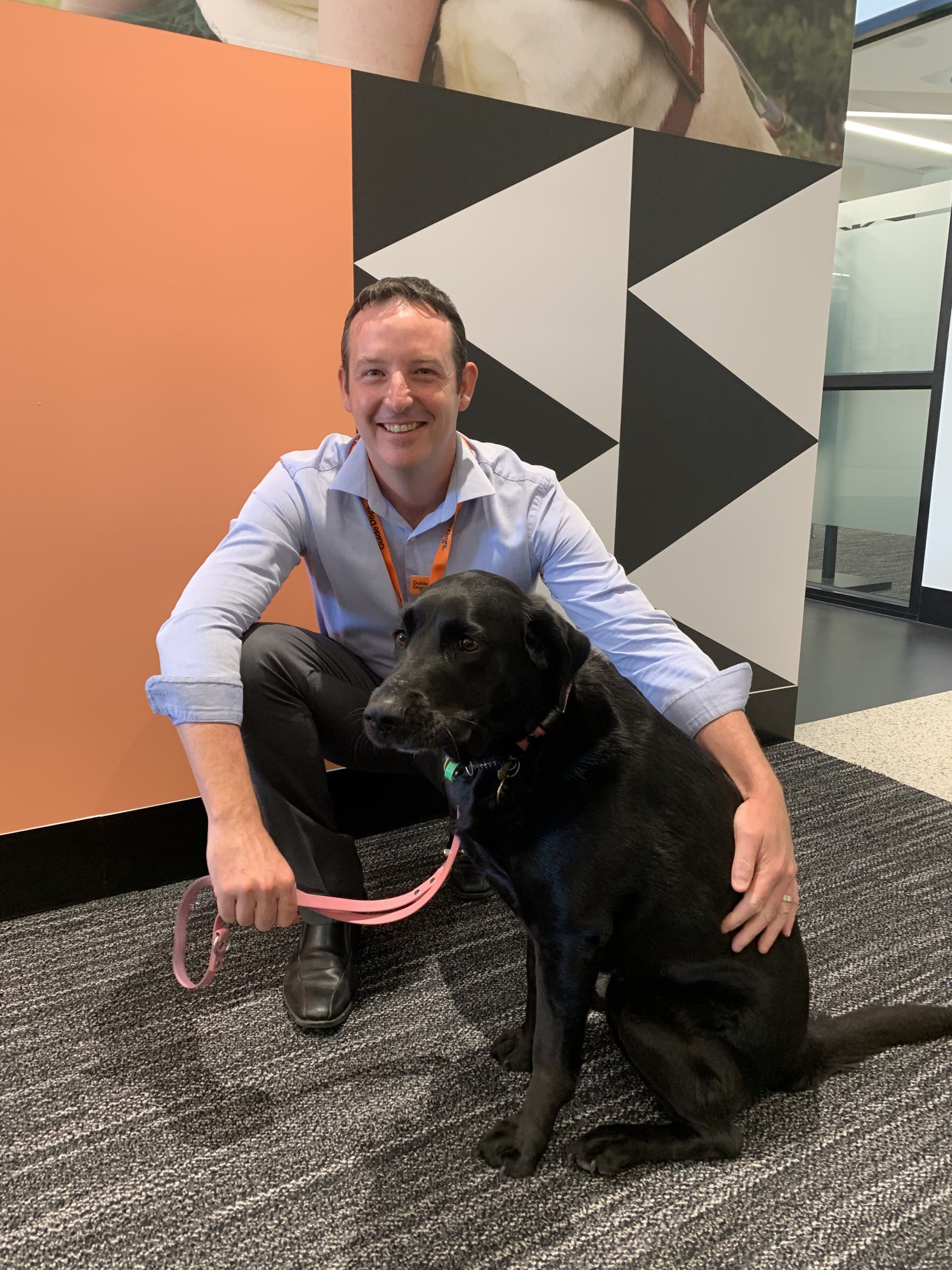 Mike kneeling down next to a black Labrador, smiling at the camera.