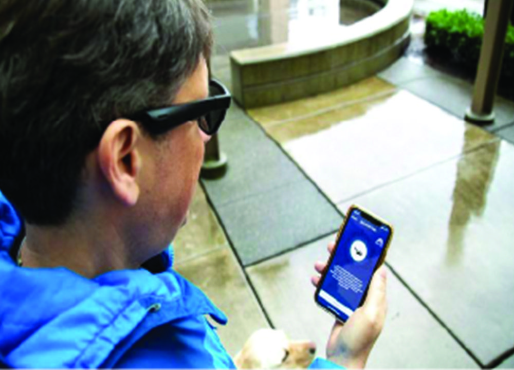 A person is standing on the sidewalk with a yellow labrador next to them. They are looking at their smartphone