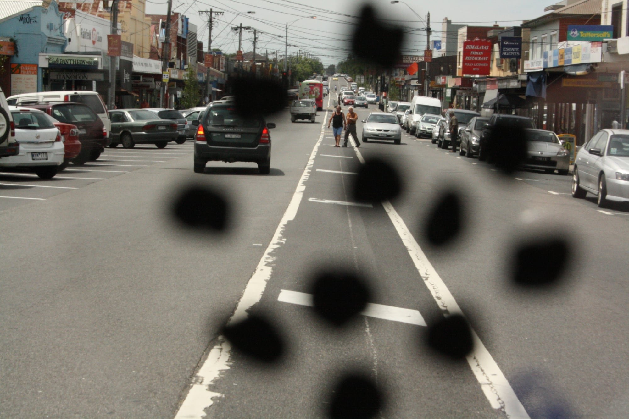 A busy road with cars on it. There are black spots on the image to portray how someone with diabetic retinopathy might view it.