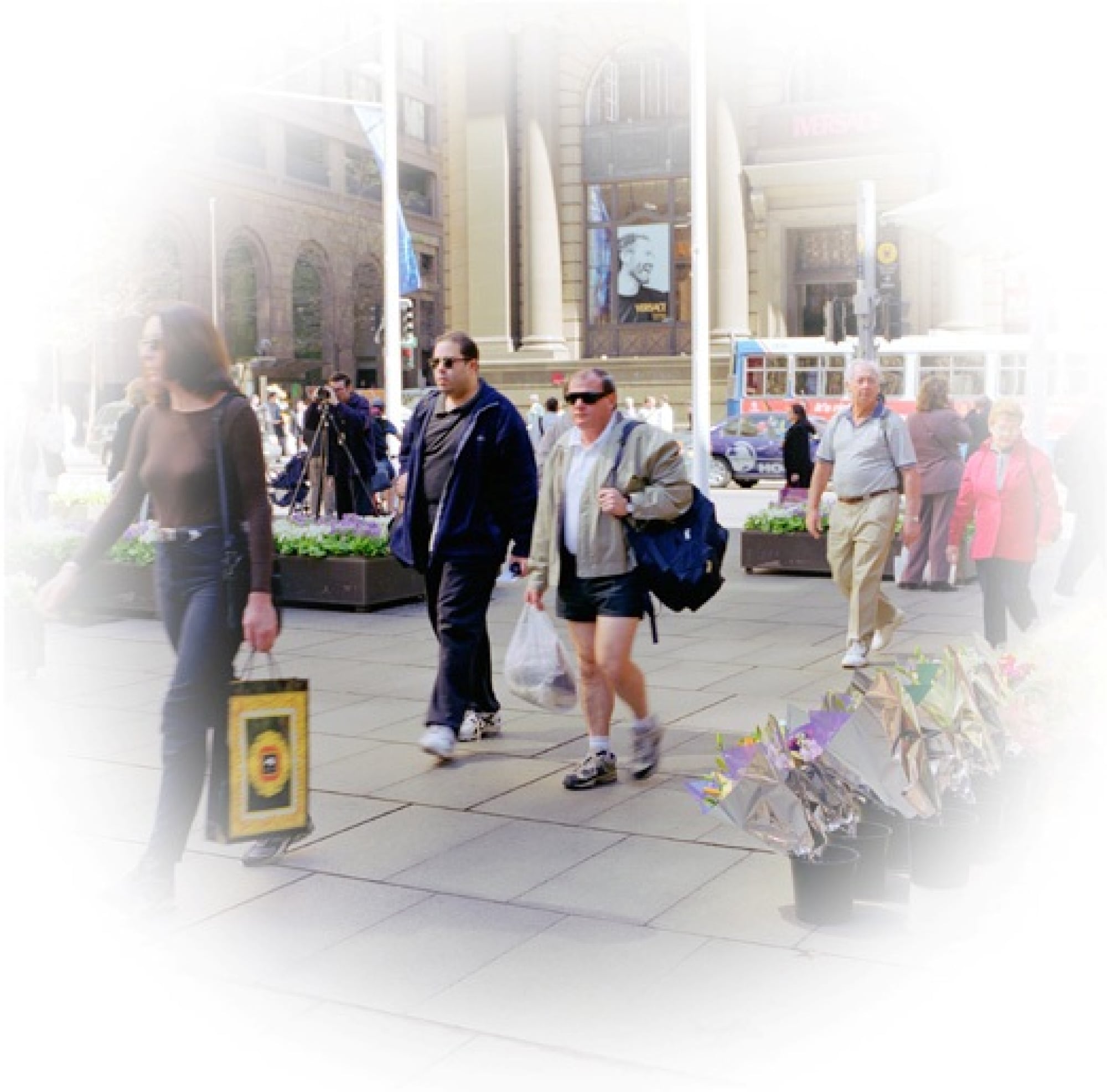 A busy footpath with people on it. The outer edges of the image is blurred with a white circle to portray how someone with Glaucoma might view it.