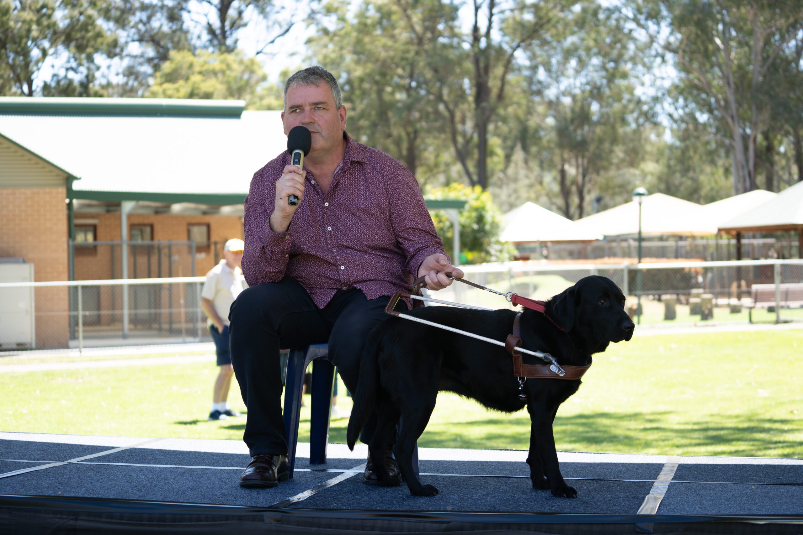 A person speaking into a microphone with their Guide Dog standing in front of them