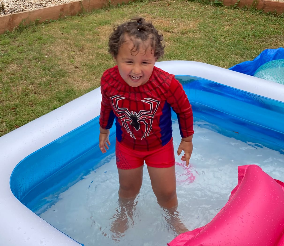 Ezra standing in an inflatable pool, smiling while wearing a Spiderman top