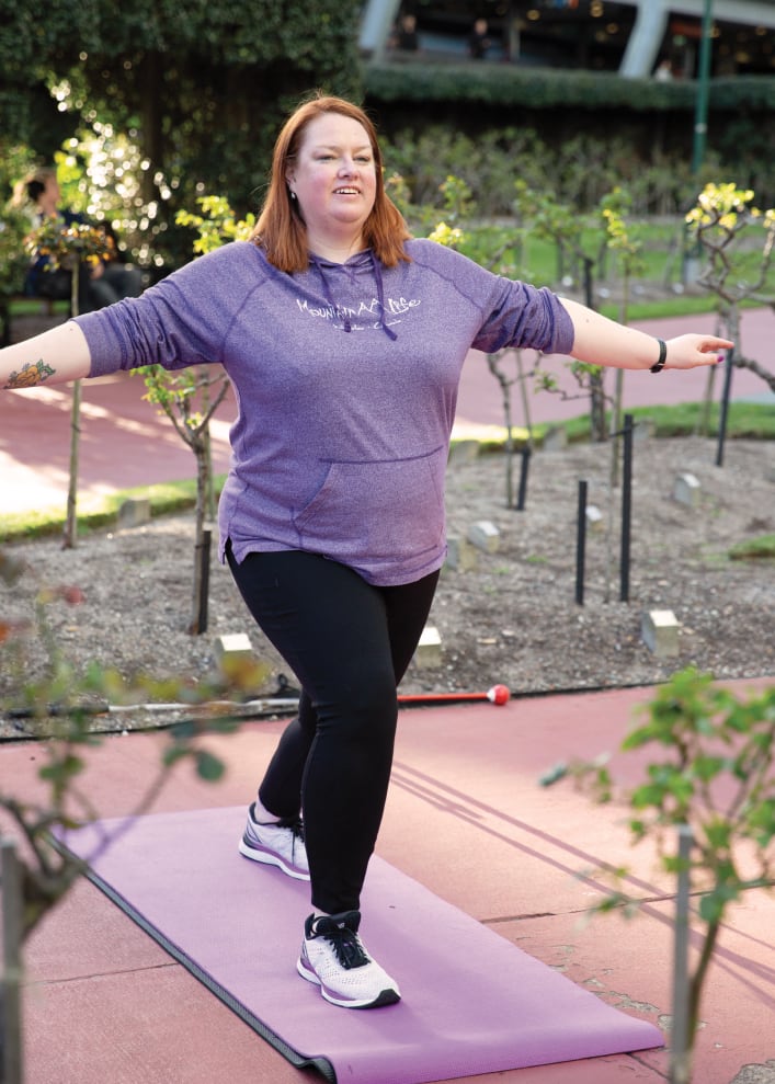 A woman doing yoga outside with her cane on the ground beside her