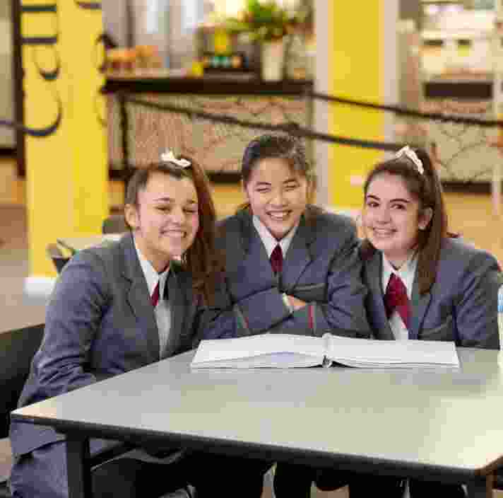 Three girls sitting at the school cafeteria, smiling.