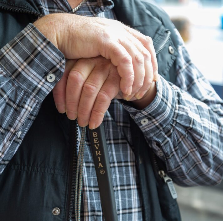 Close up of two hands resting on the top of a white cane.