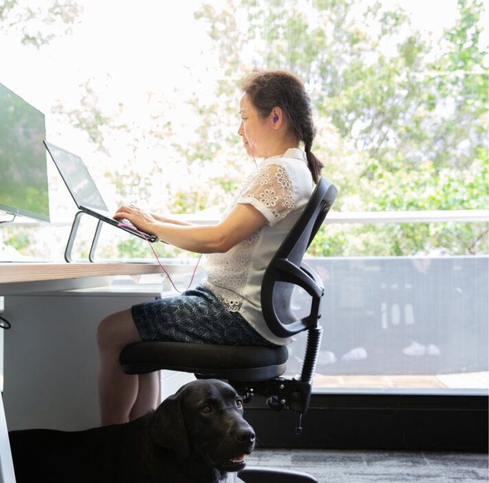 A person sitting at a desk using their laptop. The image is a profile view.