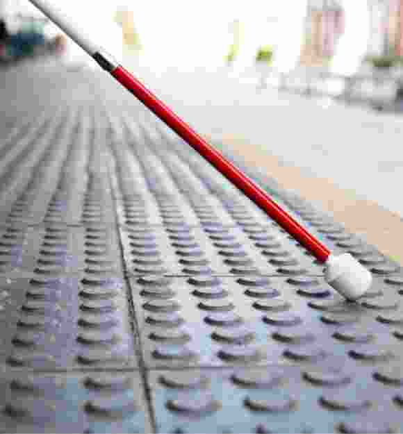 Close up image of the bottom half of a white cane on tactile tiles.