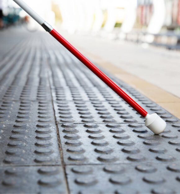 Close up image of the bottom half of a white cane on tactile tiles.
