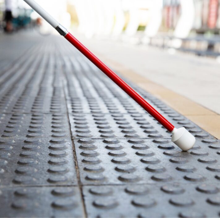 Close up image of the bottom half of a white cane on tactile tiles.