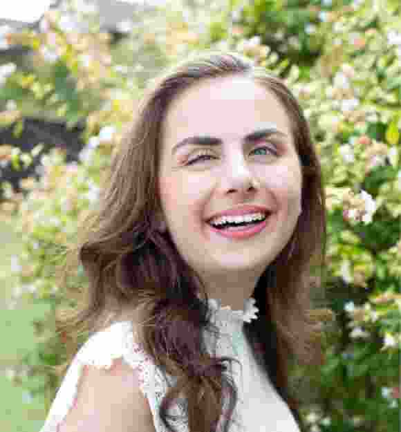 A person standing outside in a garden with a smile on their face looking at the camera.