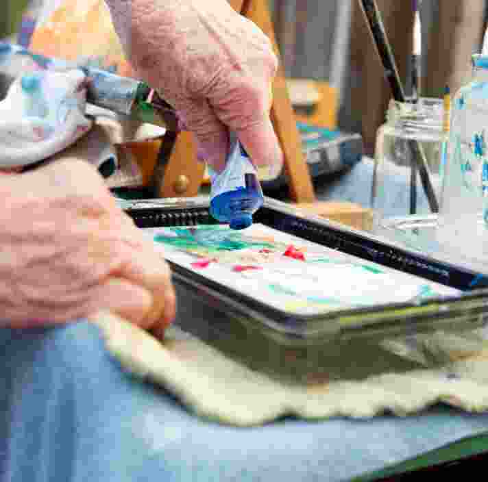 An older adult squeezing paints out of a tube into a paint tray.