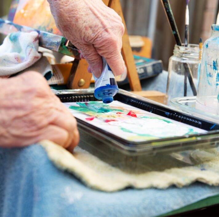 An older adult squeezing paints out of a tube into a paint tray.