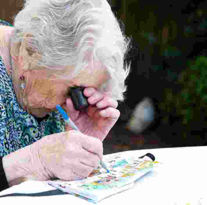 An older adult using a magnifier whilst painting, The person is painting onto a canvas.