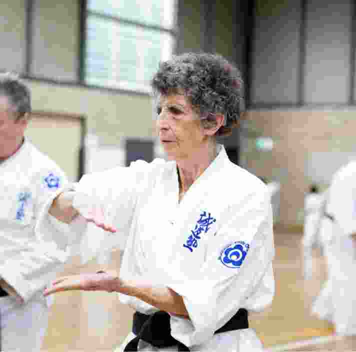 Two people at an indoor karate class. Both are in a karate uniform and are holding their hands in a karate pose.